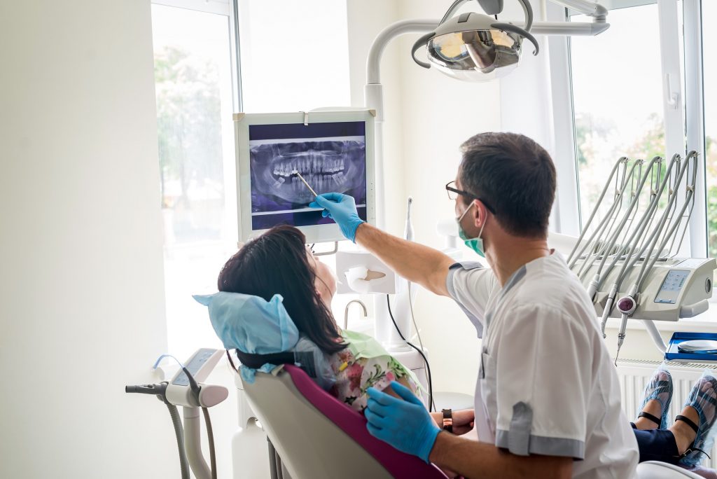 a male dentist points at a dental xray on a screen to show the patient in the chair their xray results