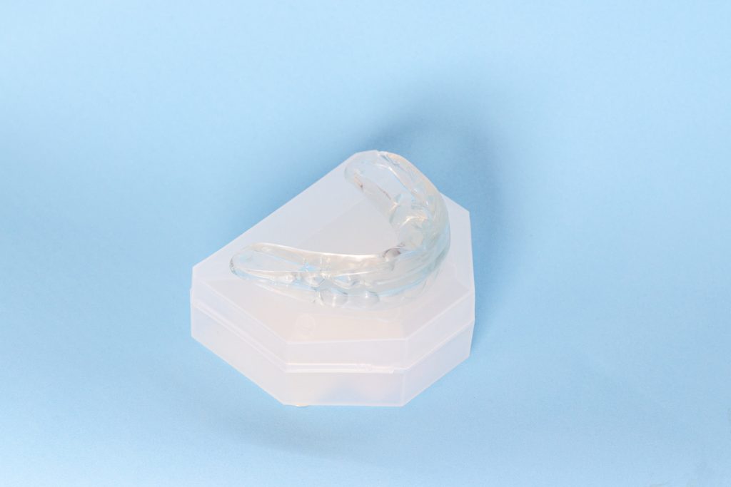 A clear mouth guard sits on a white container on a blue background