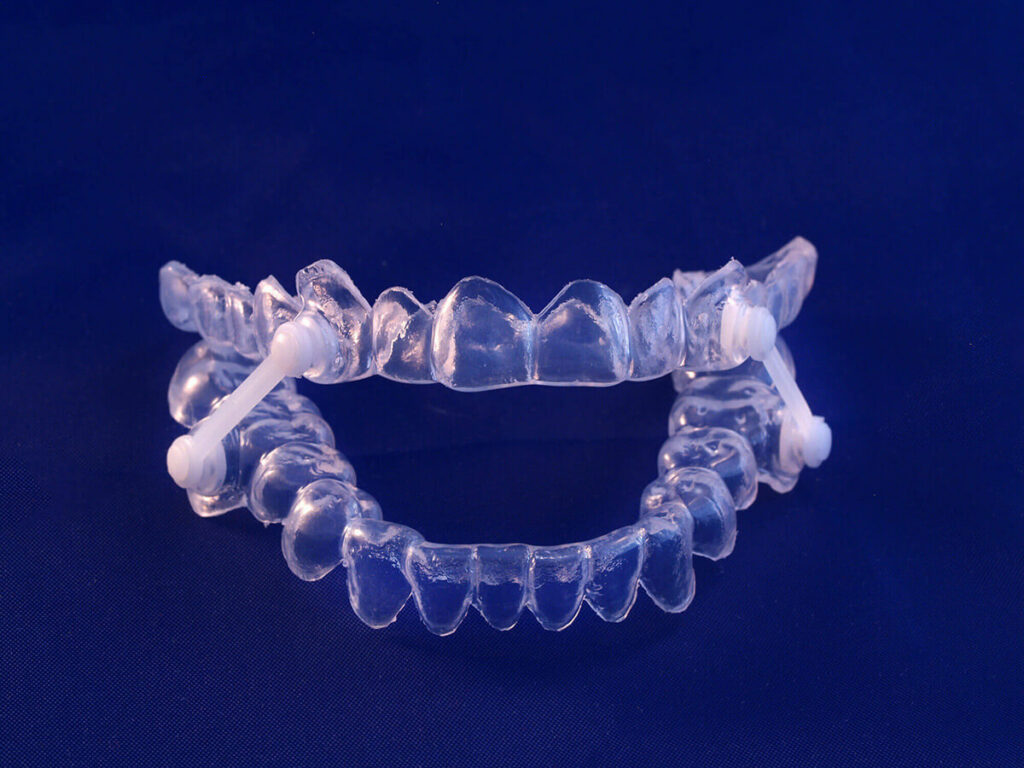 A pair of clear sleep apnea aligners with white attachments on a dark blue background.