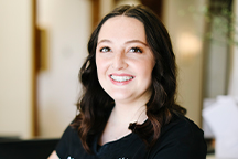 Headshot of Dakota of Haslam Dental wearing a black top with a blurred indoor background.