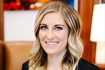 Headshot of Savana of Haslam Dental wearing a black top with a blurred indoor background.