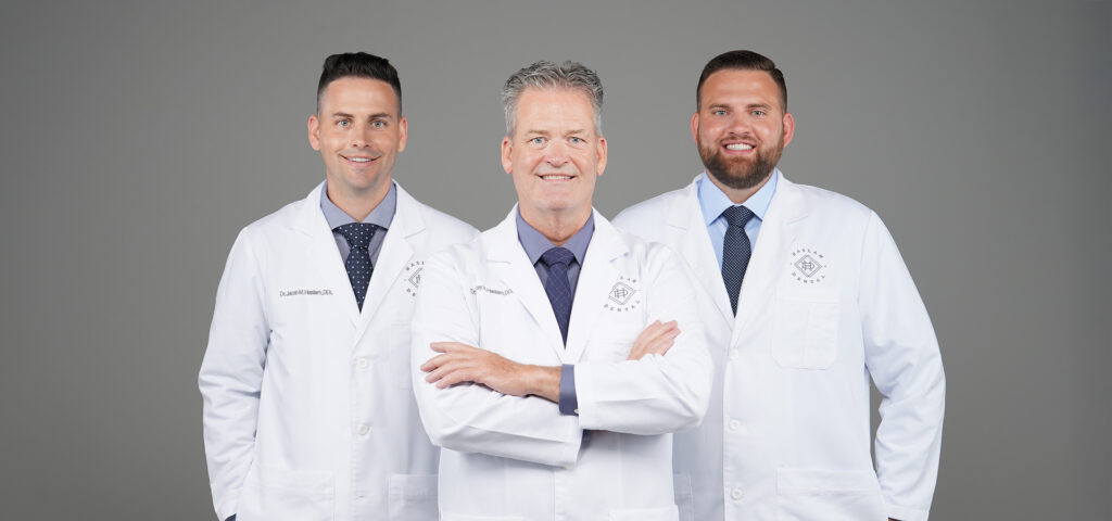 Three dentists from Haslam Dental in Ogden, Utah, smiling in white lab coats, promoting implant, cosmetic, and family dentistry.